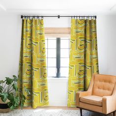 a living room with yellow curtains and a chair in front of a window that has a potted plant on it