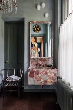 a room with a chair, mirror and chandelier hanging from the ceiling next to a window