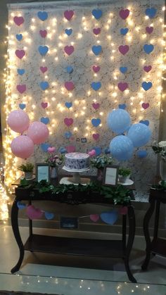 a table with balloons and decorations on it in front of a wall that is decorated with lights