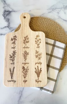 a wooden cutting board with herbs engraved on it and a dish towel next to it