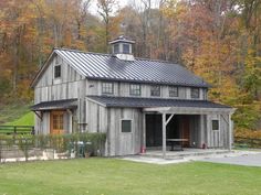 an old barn with a metal roof in the country side yard, surrounded by trees and foliage