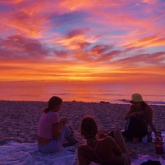 three people sitting on the beach at sunset