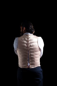 a man wearing a vest and tie standing in front of a black background with his back turned to the camera