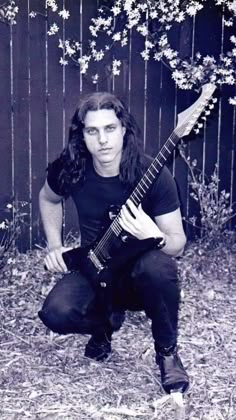 a man with long hair holding an electric guitar in front of a fence and flowers