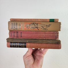 a hand holding three books in front of a white wall