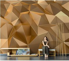 a woman is sitting on a bench in front of a wall with gold geometric shapes