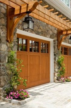 two wooden garage doors on the side of a stone building with flowers in pots below them