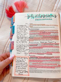 a hand holding an open bible with writing on the pages and colored paper attached to it