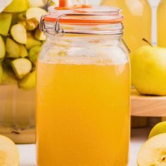 a glass jar filled with liquid next to sliced apples and other fruit in the background