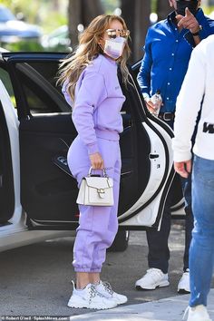 a woman in purple is getting out of a car and wearing a face mask while another man looks on