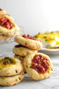 several small cookies with jam on them are sitting in front of a glass bowl and plate