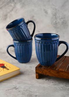 two blue coffee mugs sitting on top of a wooden table next to a book