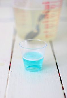 a small glass filled with blue liquid sitting on top of a white table next to a measuring cup