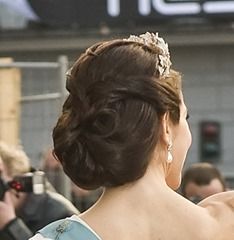 a woman wearing a tiara standing in front of a group of people with cameras