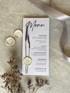 the menu card is next to some dried flowers and two waxed seals with ribbons on them