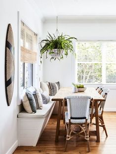 a dining room table and chairs in front of a window with plants on the windowsill