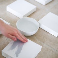 a person's hand on a piece of paper next to a bowl and square object