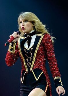 taylor swift performing on stage at an event wearing a red sequin jacket and black skirt