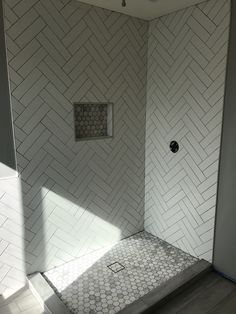 a walk in shower sitting next to a white tiled wall and floor with a window