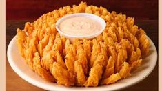 a white plate topped with fried food on top of a wooden table next to a bowl of dip