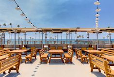 an outdoor dining area with wooden tables and umbrellas overlooking the ocean on a sunny day