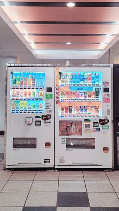 two vending machines sitting next to each other on a tiled floor in an airport