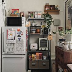 a kitchen area with a refrigerator, microwave and shelves filled with various items on top of it