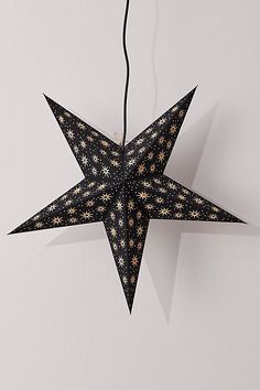 an origami star hanging from a string on a white wall with black and gold stars