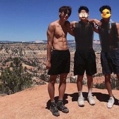 three young men standing on top of a mountain posing for a photo with an animal mask