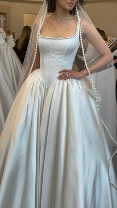 a woman in a white wedding dress with pearls on her head and veil over her shoulder