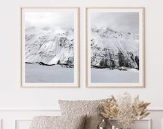 two black and white pictures hanging on the wall next to a couch with pillows in front of it