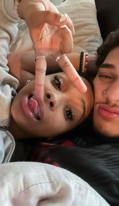 a man and woman laying on top of a bed making the peace sign with their fingers