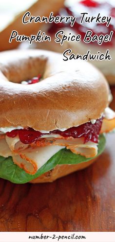 a bagel sandwich sitting on top of a wooden table next to another bagel