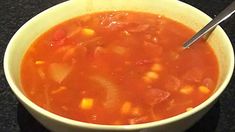 a white bowl filled with soup on top of a black counter next to a spoon