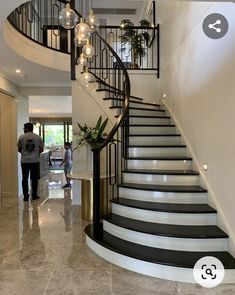 two people are walking down the stairs in a house with marble floors and black railings