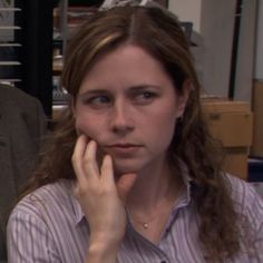 a woman is sitting in an office with her hand on her face and looking at the camera