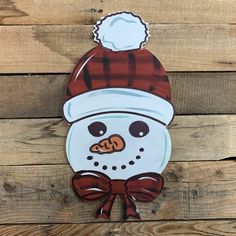 a snowman wearing a red and white hat on top of a wooden plank wall