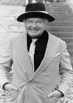 an old man in a suit and hat standing next to some steps wearing a top hat