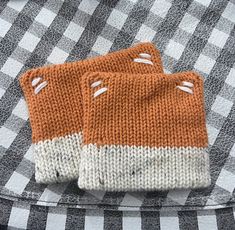 two orange and white knitted mitts sitting on top of a checkered table cloth