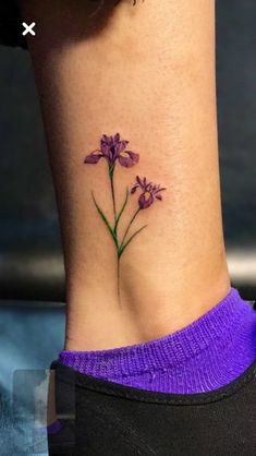 small purple flower tattoo on the side of the ankle, with green stems and leaves