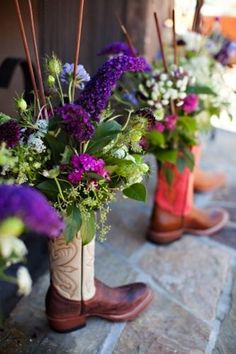 purple and white flowers are in tall boots on the stone flooring next to each other