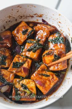 a white bowl filled with tofu and vegetables next to chopsticks in sauce