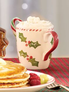 a plate topped with pancakes next to a cup of hot chocolate and a mug filled with whipped cream