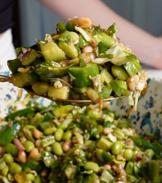 a spoon full of green vegetables being held by someone's hand over a bowl