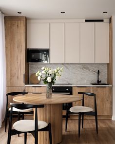 a kitchen with white cabinets and black chairs in front of a table that has flowers on it