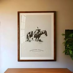 a black and white photo hangs on the wall above a wooden table with a plant