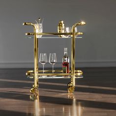 a gold bar cart with wine glasses and bottles on it, sitting on a wooden floor