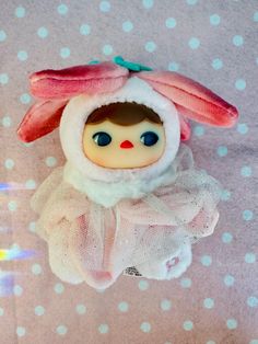 a small doll is wearing a white coat and pink ears on it's head