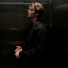 a man standing in front of an elevator with his hand on his hip and looking off to the side