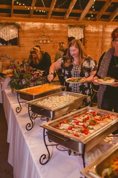 several people are serving themselves food from trays at a buffet table in a barn